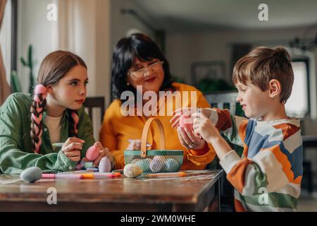 Famille décorant des oeufs de Pâques à table Banque D'Images