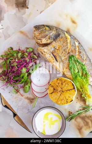 Un plat appétissant composé de poisson Dorado grillé assaisonné de zeste de citron et d'herbes aromatiques, magnifiquement présenté sur une assiette blanche. Banque D'Images