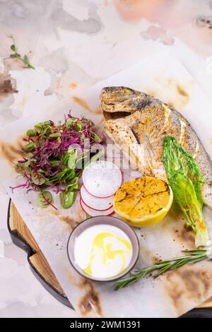 Un plat appétissant composé de poisson Dorado grillé assaisonné de zeste de citron et d'herbes aromatiques, magnifiquement présenté sur une assiette blanche. Banque D'Images