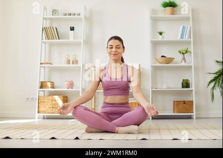 Portrait d'une jeune femme détendue faisant de l'exercice de yoga à la maison assise dans la pose de lotus. Banque D'Images