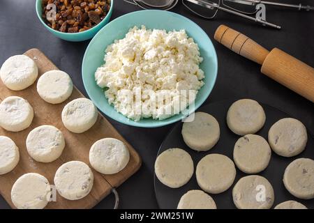 Cheesecakes à base de fromage cottage et de raisins secs. Préparez la nourriture pour le petit déjeuner. Crêpe Syrnik. Gâteau au fromage rond sur fond noir Banque D'Images