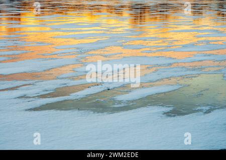 Le coucher de soleil doré se reflète sur le lac glacé, créant des teintes chaudes et une atmosphère calme. Banque D'Images