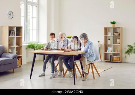 Grands-parents et petits-enfants passant du temps ensemble, assis à table et dessinant des photos Banque D'Images