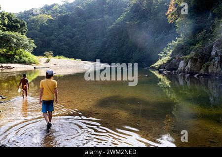 Randonneur touriste enfant traversant la rivière Pequeni avec son ami embera dans le parc national de chagres, randonnée au village embera au fond de la jungle tropicale, panama Banque D'Images