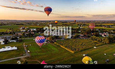 Une vue aérienne de plusieurs montgolfières survolez Un paysage pittoresque avec Un labyrinthe de maïs, une ville et des champs pendant Un coucher de soleil Golden Hour. Banque D'Images