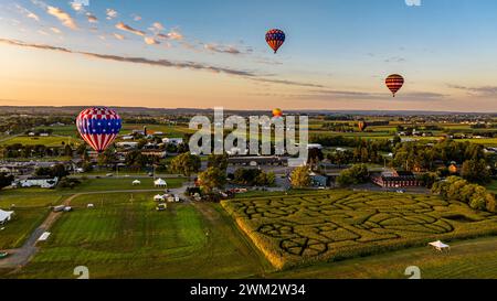 Une vue aérienne de plusieurs montgolfières survolez Un paysage pittoresque avec Un labyrinthe de maïs, une ville et des champs pendant Un coucher de soleil Golden Hour. Banque D'Images