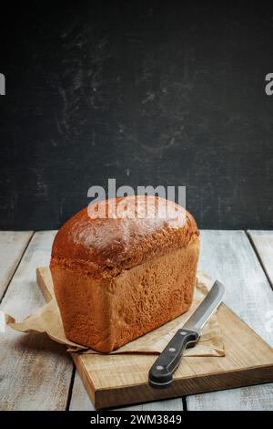Concept des méthodes traditionnelles de cuisson du pain levé. Pain entier tranché sur planche de bois rustique foncé gros plan. Pain au levain traditionnel coupé i Banque D'Images