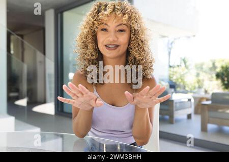 Une jeune femme biraciale fait des gestes tout en parlant à la maison sur un appel vidéo Banque D'Images