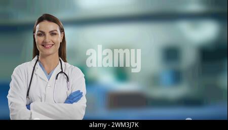 Portrait d'une femme médecin caucasienne avec les bras croisés souriant contre l'hôpital en arrière-plan Banque D'Images