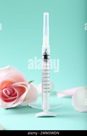 Cosmétologie. Seringue médicale, fleur de rose et pétales sur fond turquoise Banque D'Images