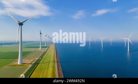 Une vue aérienne d'un parc éolien sur une plaine au milieu de l'océan, avec des éoliennes s'étendant vers le ciel, se fondant dans le paysage naturel de l'eau et des nuages Banque D'Images