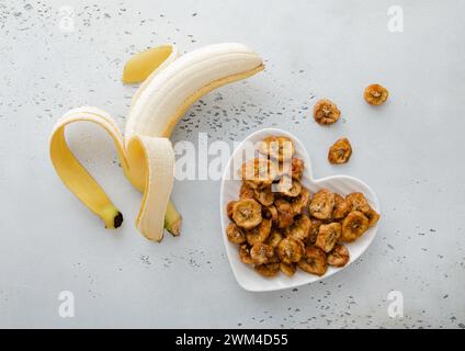 Tranches de bananes séchées dans une assiette en forme de coeur avec banane crue sur Ligh board.Macro Banque D'Images