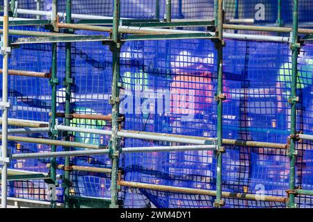 Ouvriers de la construction derrière la maille bleue et l'échafaudage sur le chantier de construction de grande hauteur. Banque D'Images