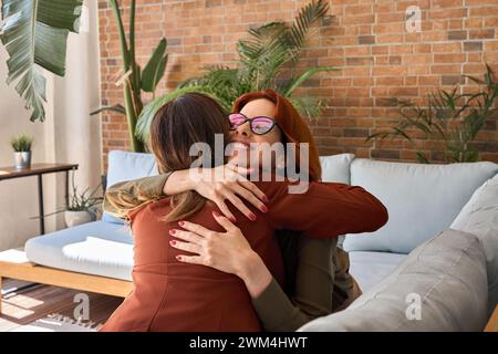 Deux femmes d'affaires heureuses assis sur le canapé au travail dans le bureau et câlins. Banque D'Images
