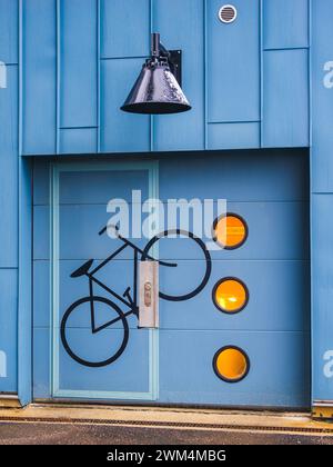 Un mur d'entrepôt bleu vif à Gothenburg, en Suède, présente une silhouette peinte d'un vélo et trois panneaux circulaires orange. Le dessin sugg Banque D'Images