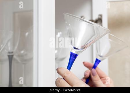 la main d'une femme sort un verre à martini de l'armoire. armoire de cuisine avec vaisselle. videz le verre à martini. alcoolisme féminin. verre à cocktail Banque D'Images