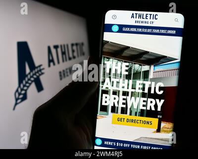 Personne tenant le téléphone portable avec la page Web de la société américaine de boissons Athletic Brewing Company devant le logo. Concentrez-vous sur le centre de l'écran du téléphone. Banque D'Images