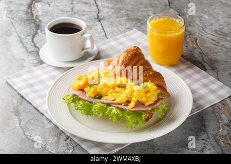 Sandwich aux œufs brouillés avec jambon, oignons verts et laitue servi avec jus d'orange et café gros plan sur une table en marbre. Horizontal Banque D'Images