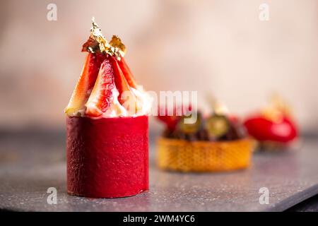 Tarte au chocolat gourmande, mousse à la fraise, macaron à la framboise sur planche en ardoise avec fond rose pour un élégant affichage de dessert. Banque D'Images