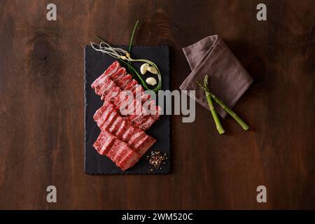 viande de boeuf crue sur plaque de pierre noire avec de l'ail et de la ciboulette sur fond en bois Banque D'Images