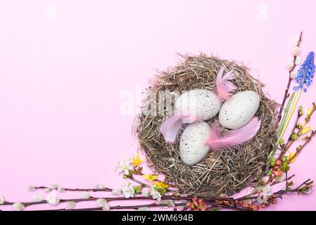 Nest mit gepunkteten Ostereiern und Blütendekoration vor pinkem Hintergrund Banque D'Images