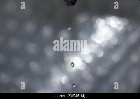 Petites gouttes d'eau sortant du robinet goutte à goutte avec fond lumineux horizontal Banque D'Images