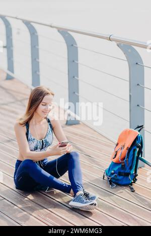 Femme détendue avec des écouteurs sur une promenade en bord de mer en utilisant son téléphone portable. Banque D'Images