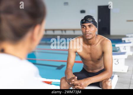 Un jeune athlète masculin biracial nageur écoute attentivement au bord de la piscine Banque D'Images