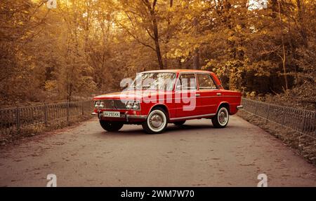 Berline VAZ 2103 classique des années 1970 sur route forestière. Red Lada tourné pendant l'heure dorée - vue de trois quarts de face. Banque D'Images