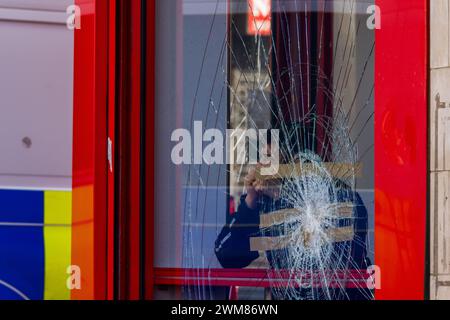 Bradford, Royaume-Uni. 24 FÉVRIER 2024. Un client regarde depuis Salah's Takeaway sur Leeds Road tandis que la marche du West Yorkshire pour la Palestine passe en chantant vers le magasin. On peut encore voir que la boutique a été endommagée suite à une violente confrontation entre les propriétaires de magasins et les manifestants pro-palestiniens la nuit précédente suite à un conflit de boycott. Une camionnette de police est en arrière-plan. Crédit Milo Chandler/Alamy Live News Banque D'Images