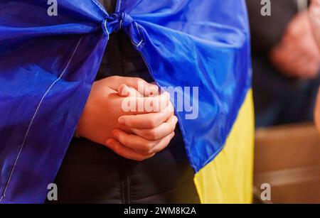 24 février 2024, Hesse, Francfort-sur-le-main : un homme avec un drapeau ukrainien tient les mains pliées dans la prière. Une prière œcuménique pour l'Ukraine a eu lieu en préparé La cathédrale de Barthélemy sous le titre « la lumière prévaudra sur les ténèbres ». Par la suite, les gens se sont commémorés avec des bougies sur la place de la cathédrale. Photo : Andreas Arnold/dpa Banque D'Images