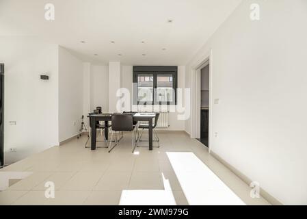 Salon d'une maison unifamiliale avec des murs lisses peints en blanc, une table à manger en bois noir avec des chaises et menuiserie en métal en aluminium noir et gl Banque D'Images