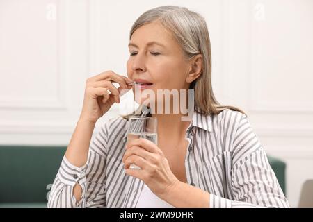 Ménopause, hormonothérapie substitutive. Femme avec un verre d'eau prenant la pilule à la maison Banque D'Images