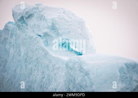 Un des icebergs massifs du fjord glacé à Illulisat, Groenland, montrant de la neige texturée blanche et turquoise et deux yeux. Banque D'Images