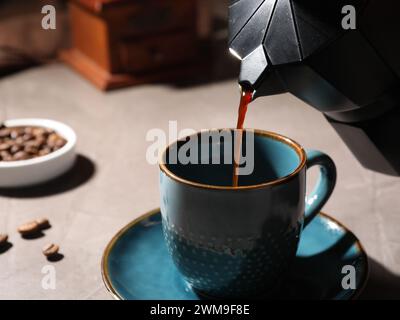 Verser le café aromatique du pot de moka dans la tasse à la table lumineuse, gros plan Banque D'Images