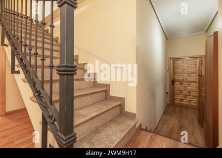 Escalier intérieur d'une maison résidentielle en duplex avec marches en tuiles grises, balustrade en métal et porte d'accès en bois lambrissée de style castillan Banque D'Images