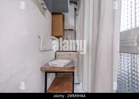 Un petit balcon terrasse avec fenêtres en métal et portes en verre et en aluminium, une machine à laver et un chauffe-eau Banque D'Images