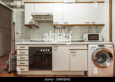 Image avant de la cuisine meublée avec des meubles blancs anciens avec des poignées en bois, armoire avec plusieurs tiroirs, four à micro-ondes sur le comptoir blanc Banque D'Images