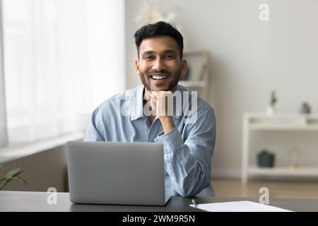 Homme indien assis à son bureau avec son ordinateur portable regardant la caméra Banque D'Images