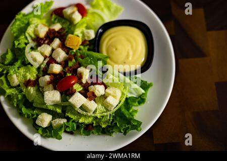 Salade César avec croûtons, œufs de caille, tomates cerises et poulet grillé dans une assiette blanche sur une table en bois foncé Banque D'Images