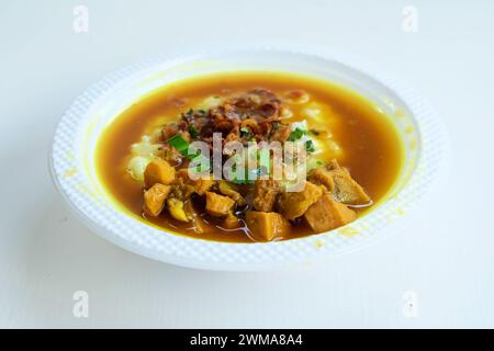 Délicieuse cuisine indonésienne à base de porridge de poulet servie dans un bol avec des plats d'accompagnement traditionnels sur fond blanc Banque D'Images