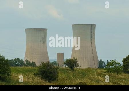 Deux tours de refroidissement industrielles hautes sur un champ vert vibrant, entourées d'une végétation luxuriante sous un ciel bleu clair. Banque D'Images