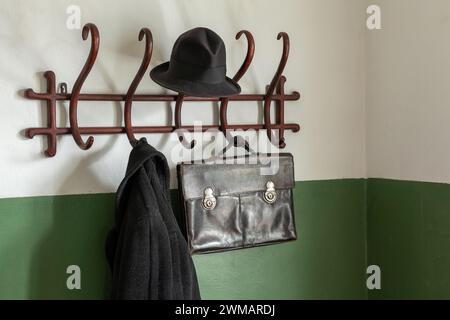 Mallette en cuir ancien noir, chapeau noir et manteau sur le cintre en tissu en bois vintage. Banque D'Images