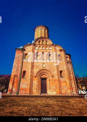 Une église en briques rouges avec une tour cylindrique, des portes voûtées et des fenêtres circulaires sous un ciel bleu clair. Église du vendredi à Chernihiv. Banque D'Images