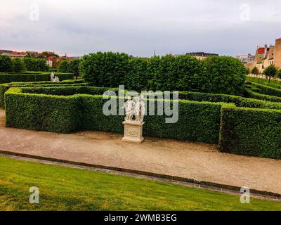 Un jardin avec des haies bien entretenues, deux statues blanches, des chemins de gravier, et un ciel nuageux. haie et sculpture dans le parc, sculptures blanches dans le parc sur th Banque D'Images