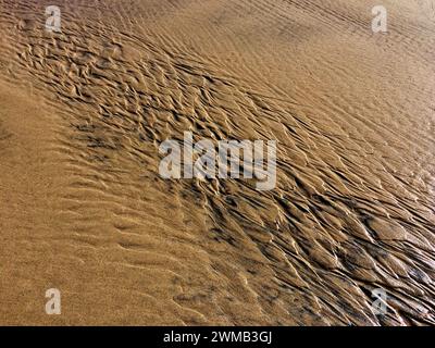 L'image capture un gros plan de sable avec des motifs complexes formés par l'écoulement de l'eau. Banque D'Images