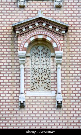 Fenêtre en treillis de pierre avec tracés complexes, encadrée par d'élégantes colonnes blanches et sertie dans un contexte de briques rouges soigneusement disposées, ornée de o Banque D'Images