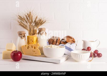 Un fromage différent, du pain, du fromage cottage, de la crème sure, du lait dans des bouteilles sur un comptoir en bois blanc. Concept de la fête juive de Shavouot Banque D'Images