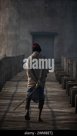 Un homme traverse le pont un matin d'hiver tenant un bâton de bambou Banque D'Images