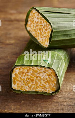 un tas de tempeh cru enveloppé dans des feuilles de banane. Le tempe est un aliment typiquement indonésien à base de soja fermenté et de plusieurs autres ingrédients Banque D'Images